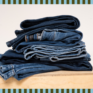 A stack of folded jeans in varying washes, neatly piled on a wooden surface against a neutral background.