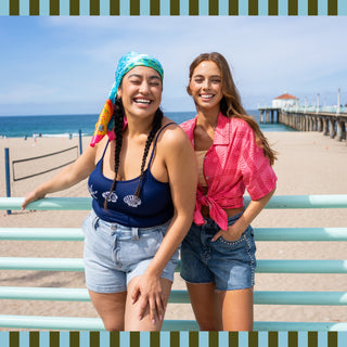 Two women smiling while wearing Judy Blue at the beach. The photo is being used to promote new shorts for summer.